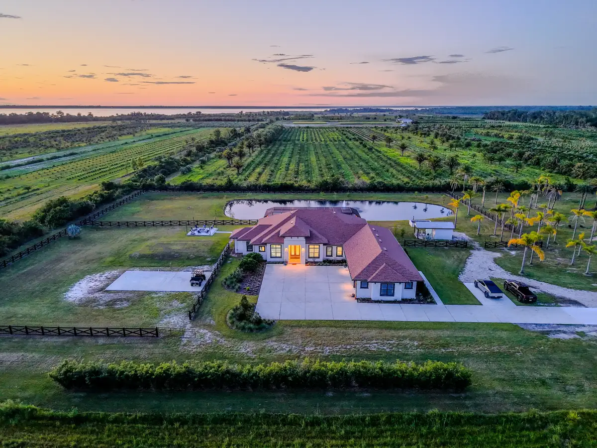 Aerial twilight view of a single-story country estate with pond, paddock, and grove