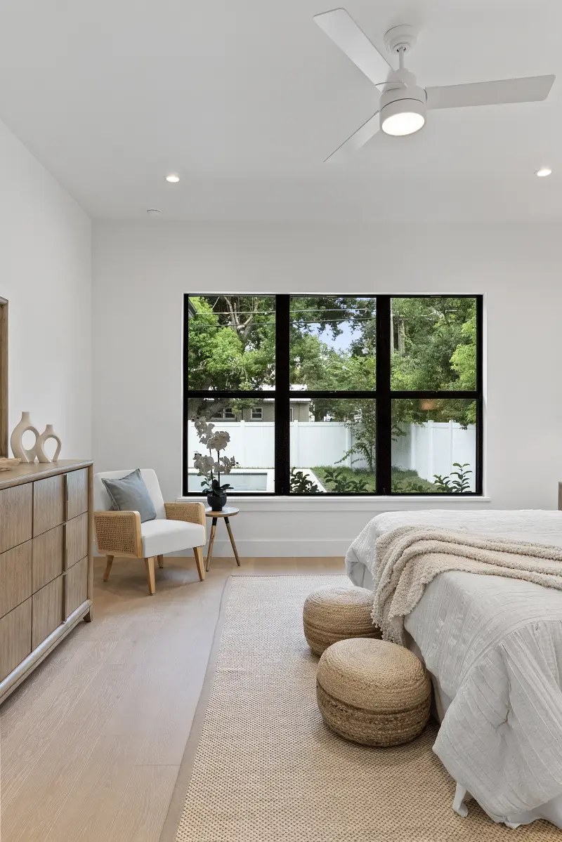 Bedroom with a dresser and a large black grid window overlooking the garden