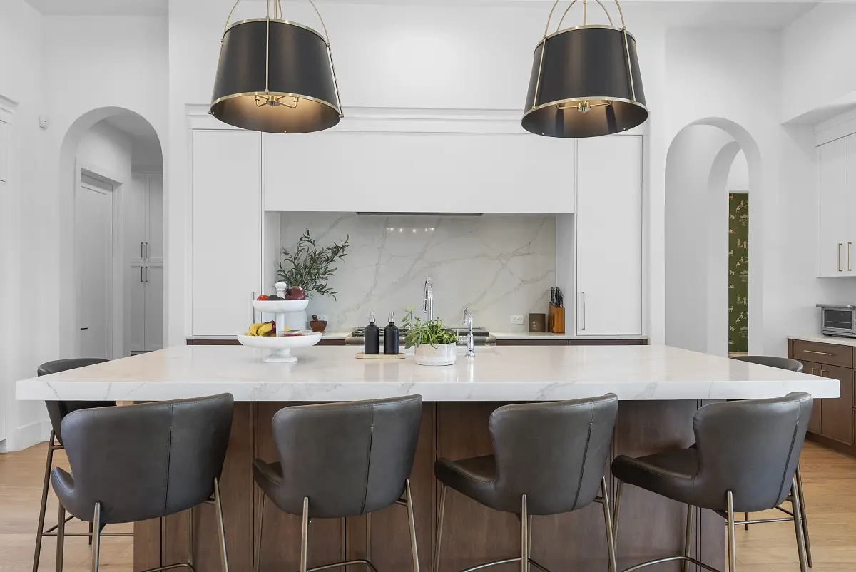 Bright white kitchen with marble backsplash, black drum pendants, and a waterfall island