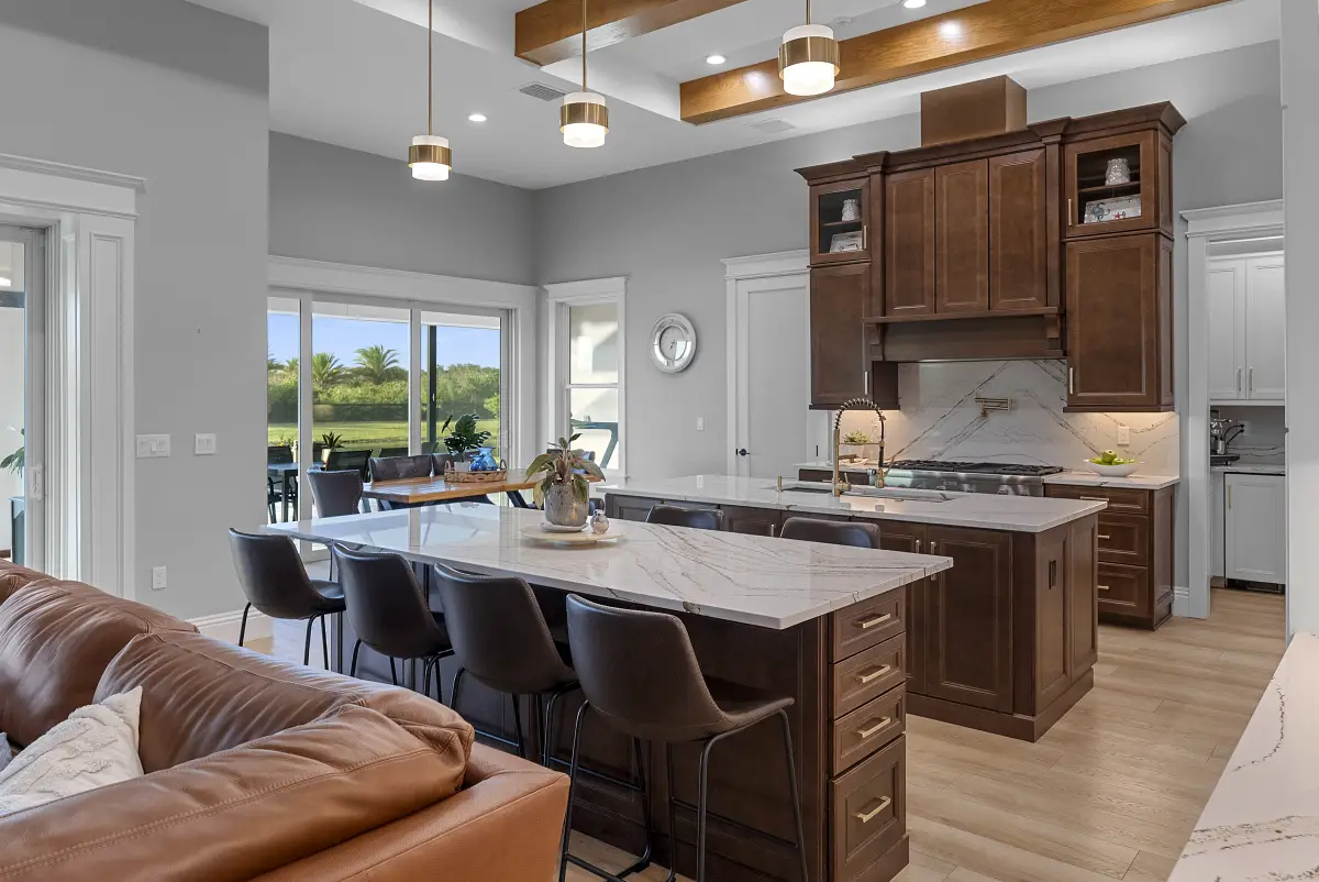 Open-plan kitchen with marble waterfall island, custom wood cabinetry, and adjoining great room