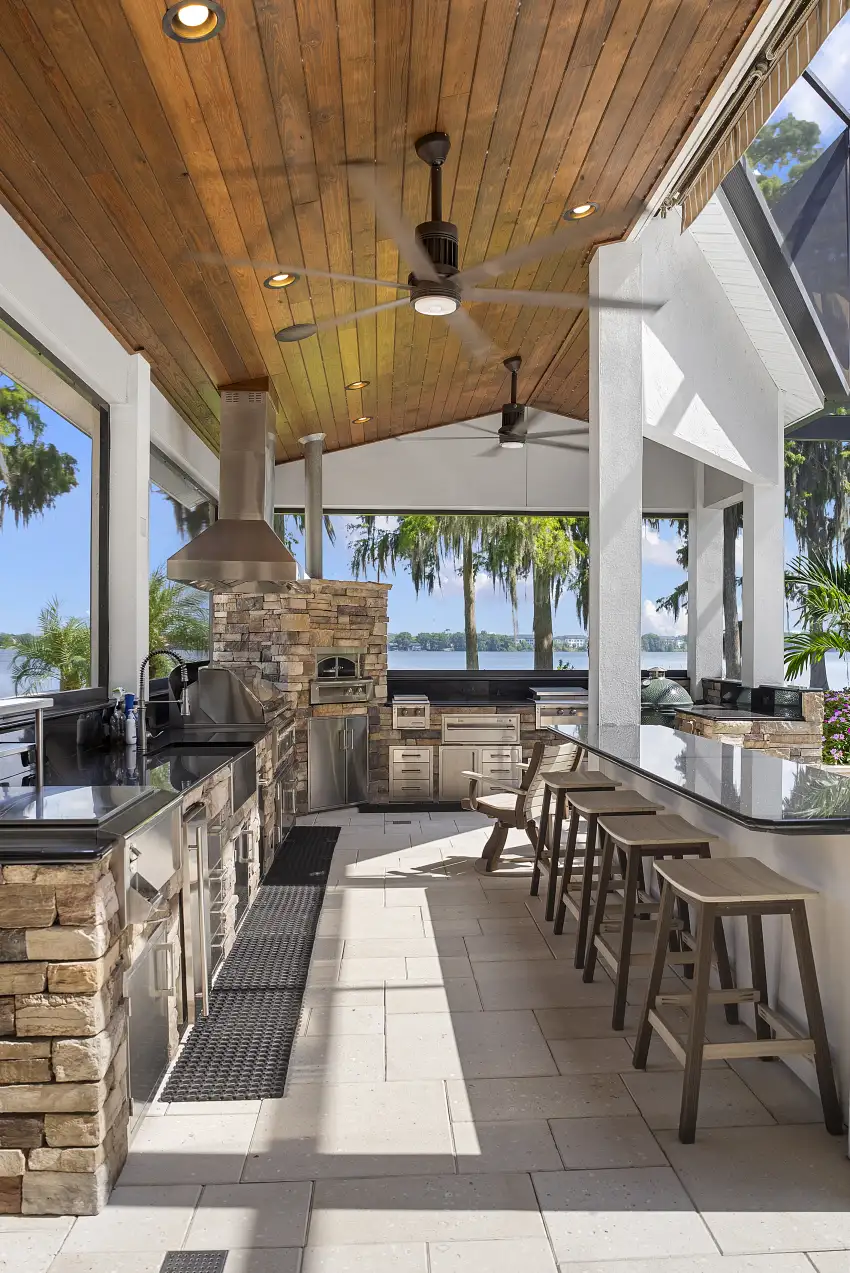 Covered outdoor kitchen with a wood ceiling and bar seating overlooking the lake